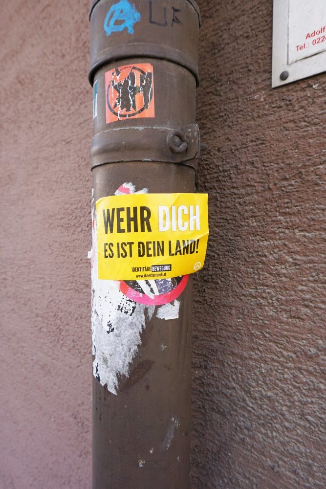 Aufkleber der Identitären und der Sozialistischen Jugend auf einer Regenrinne in der Baumgasse, Wien, 3. Bezirk
