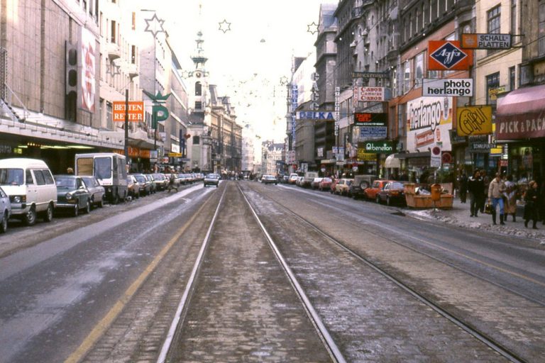 Mariahilferstraße mit Autoverkehr, Parkplätzen und Straßenbahnschienen, bei der Stiftgasse, Stiftskirche, Wien