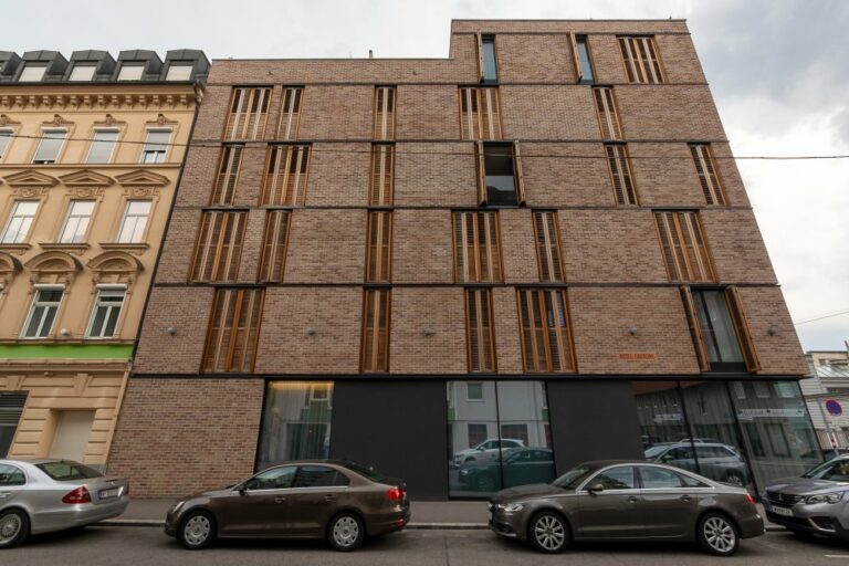 Neubau des Hotels Caroline in Favoriten, Wien, Sichtziegel, schmale Fenster, Glas im Erdgeschoß, davor parkende Autos