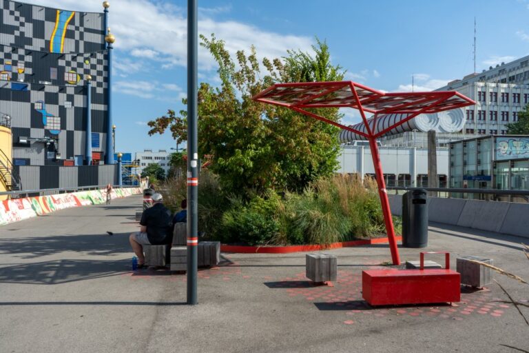 zwei Leute sitzen im Schatten auf der Fußgängerbrücke beim Bahnhof Spittelau