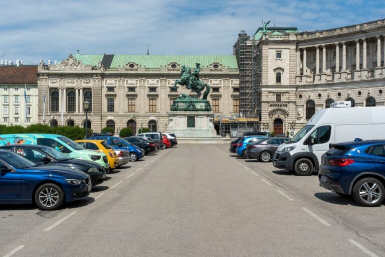 parkende Autos vor einem Denkmal auf einem Platz mit historischer Architektur