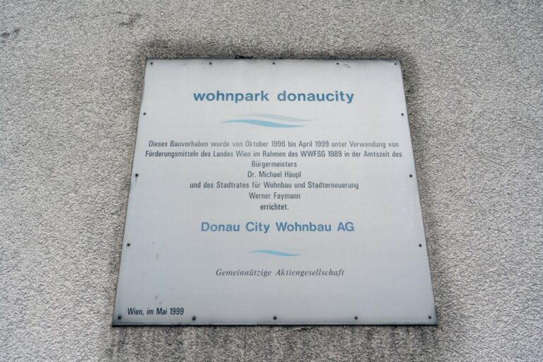 Plakette "wohnpark donaucity", "Dieses Bauvorhaben wurde von Oktober 1996 bis April 1999 unter Verwendung von Fördermitteln des Landes Wien im Rahmen des WWFSG 1989 in der Amtszeit des Bürgermeisters Dr. Michael Häupl und des Stadtrates für Wohnbau und Stadterneuerung Werner Faymann errichtet"