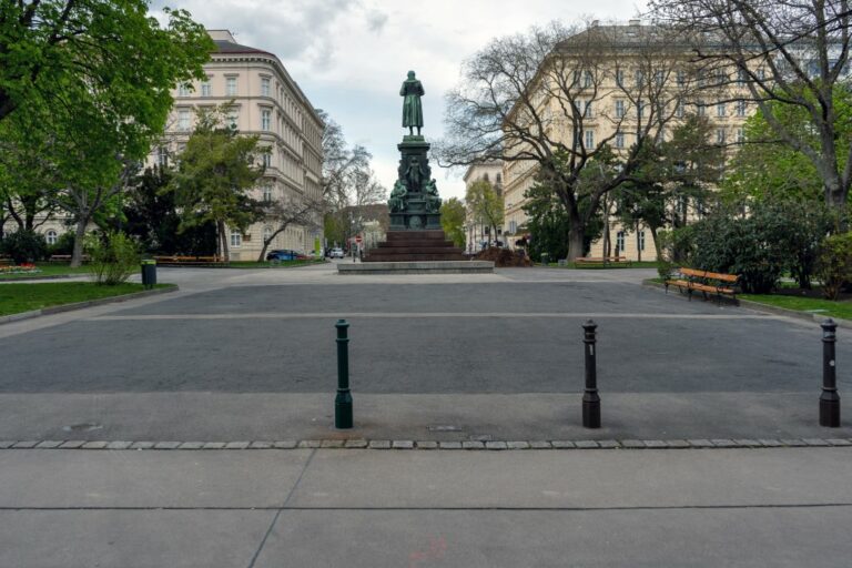 Denkmal in der Mitte eines alten Stadtplatzes, links und rechts Bäume