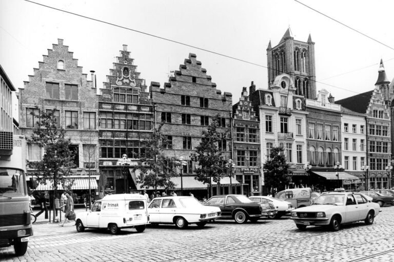 Autos vor einer Häuserzeile, hinten ein Kirchturm