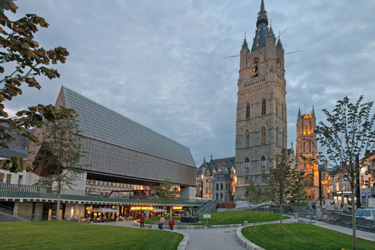 Platz und Grünflächen vor einem historischen Turm in Gent, links eine moderne Veranstaltungshalle