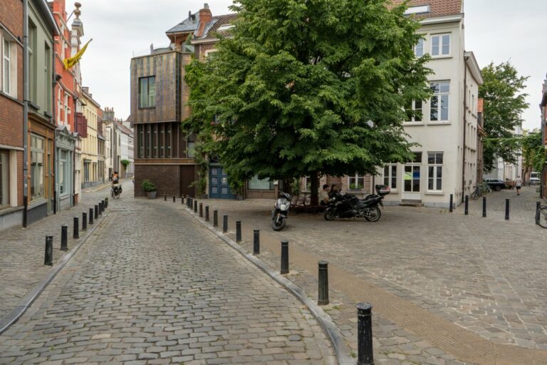 kleiner Platz und Gassen in der Altstadt von Gent, Baum, kleine Wohnhäuser, gepflasterte Straßen und Gehsteige, Poller, abgestellte Motorräder