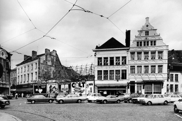 alte Häuser im Zentrum von Gent, davor parkende Autos auf Kopfsteinpflaster, Baulücke mit Plakaten davor, Oberleitungen