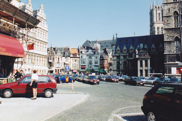 parkende Autos auf einem historischen Stadtplatz, rechts Tuchhalle und Belfried (Turm)