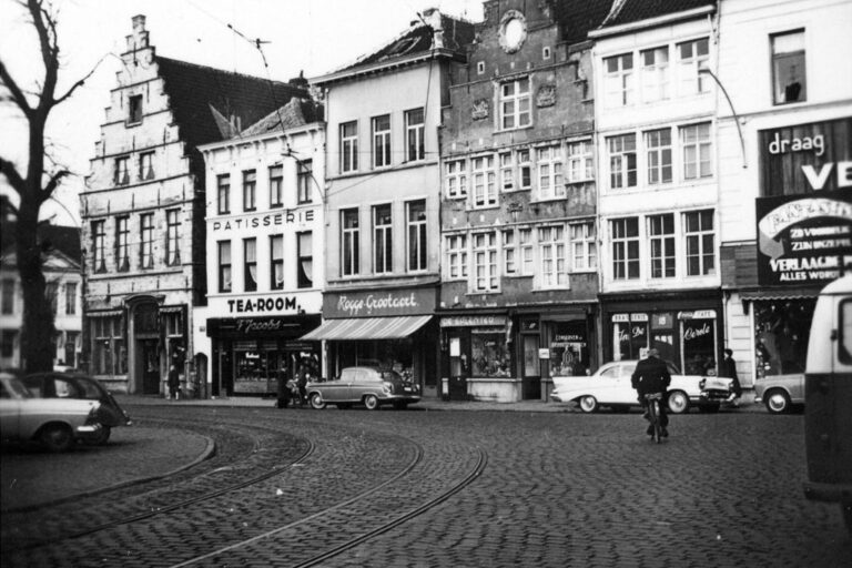 Platz in Gent mit Geschäften, davor Autos, ein Radfahrer und Straßenbahnschienen