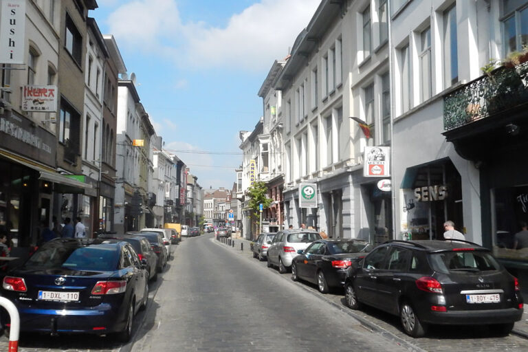 Straße mit links und rechts parkenden Autos und niedrigen Häusern