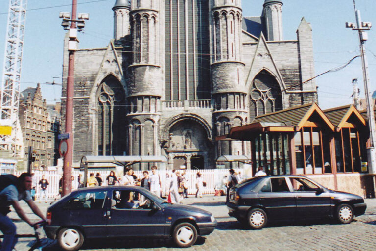Autos, Radfahrer und Haltestelle vor dem Portal einer Kirche (Parochiekerk Sint-Niklaas)