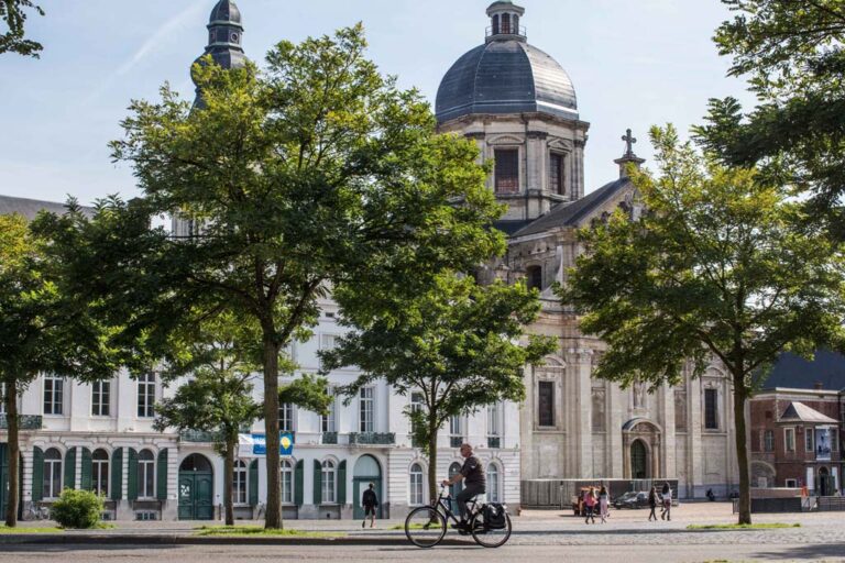 Radfahrer fährt über einen Platz in Gent, im Hintergrund historische Gebäude, Abtei mit Kuppel, Bäume