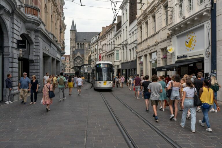 Straßenbahn fährt durch eine Fußgängerzone, links und rechts Fußgänger, vorne die Sint-Niklaaskerk (Kirche)