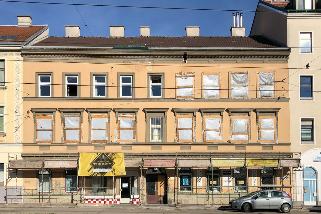 Altbau in Wien-Hernals mit herausgenommenen Fenstern und Schutzgerüst über dem Gehsteig, Schaden am Gesims