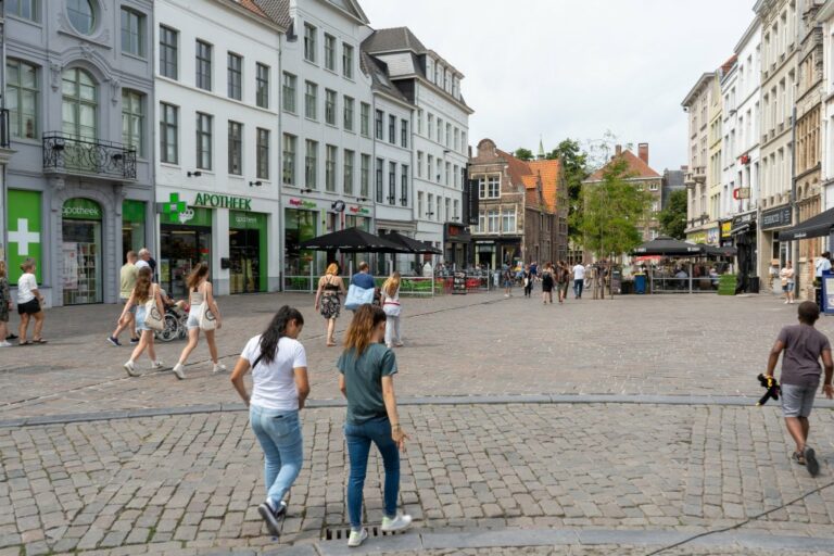 Leute gehen durch eine Fußgängerzone neben dem Vrijdagmarkt, Häuser, gepflasterter Boden, Altstadt in Belgien