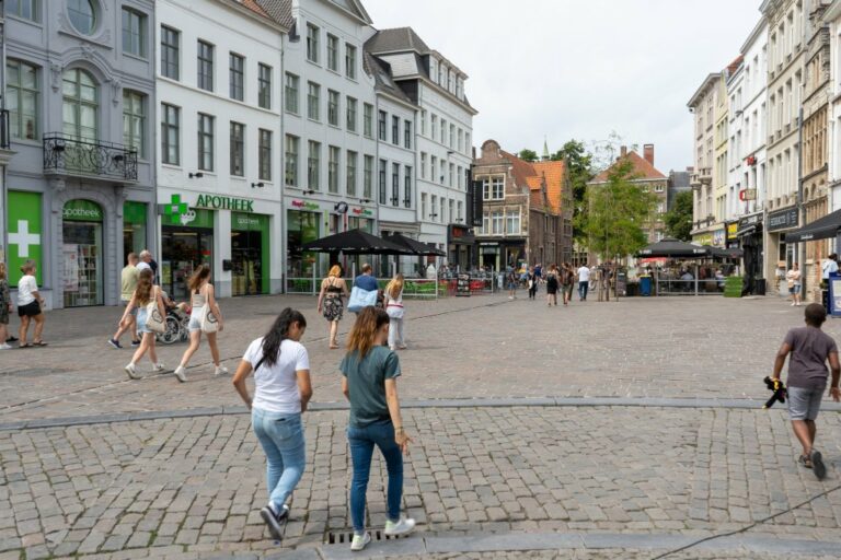 Leute gehen durch eine Fußgängerzone neben dem Vrijdagmarkt, Häuser, gepflasterter Boden, Altstadt in Belgien