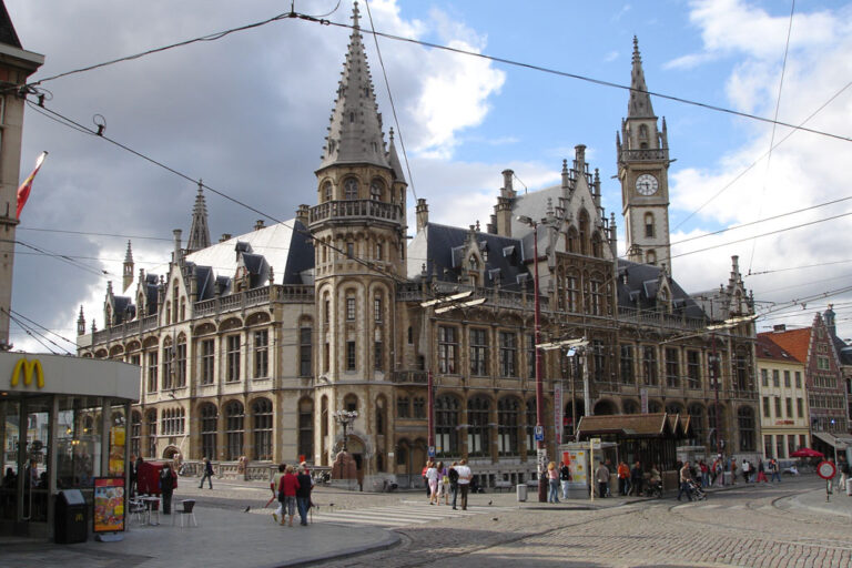 historisches Gebäude in der Altstadt von Gent, Neugotik, Uhrturm, davor Platz mit Schienen und Oberleitungen