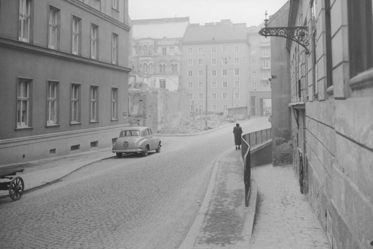 alte Aufnahme von Wien-Landstraße, in der Mitte ein kriegszerstörtes Gebäude, hinten ein Gemeindebau (errichtet 1952), links ein Gründerzeithaus mit vereinfachter Fassade und ein Auto, eine Frau geht am Gehsteig