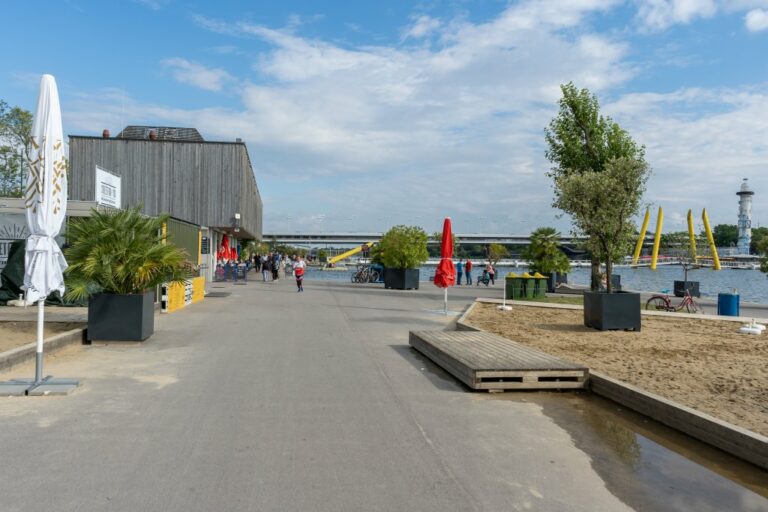 Donauufer in Wien, Sand, Asphalt, Bäume, Restaurant, Gebäude, Brücke, Sonnenschirm, Leute