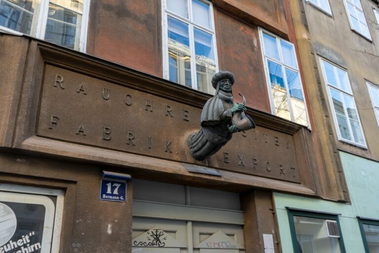 Skulptur eines pfeifenrauchenden Mannes auf dem Biedermeierhaus in der Hermanngasse 17 in Wien-Neubau, Aufschrift: "Rauchrequisiten, Fabrik, Export"