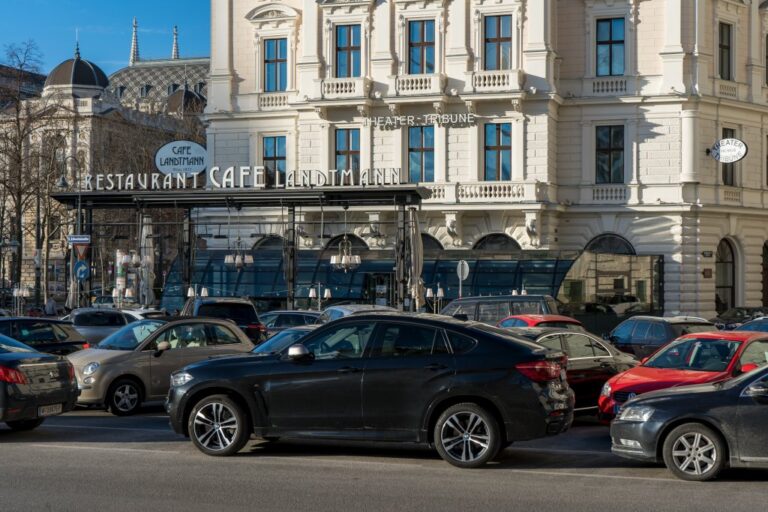 parkende Autos vor einem Kaffeehaus in Wien, dahinter das Hauptgebäude der Universität Wien am Universitätsring