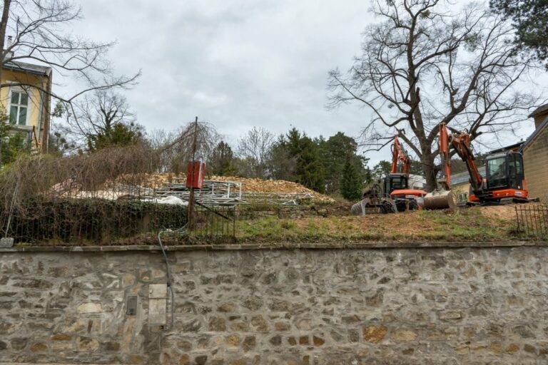 Abrissbagger, Mauer, Bäume, Grünfläche