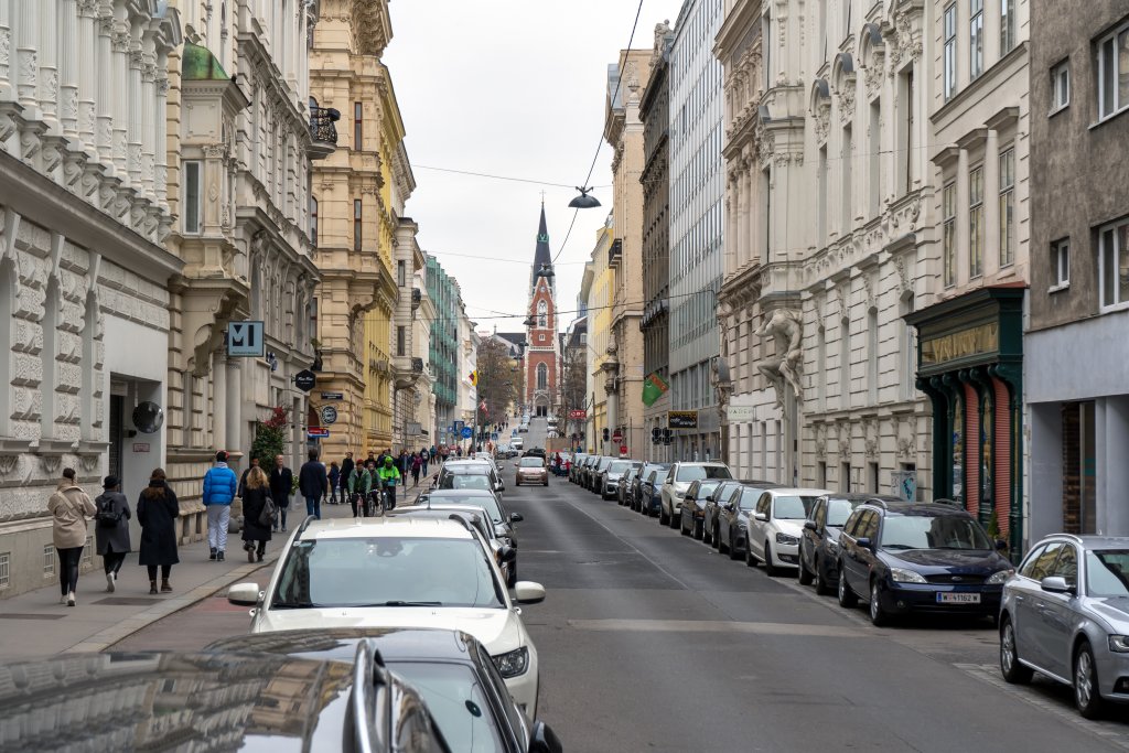 Fußgänger, Radfahrer, parkende Autos und fahrendes Auto in der Argentinierstraße