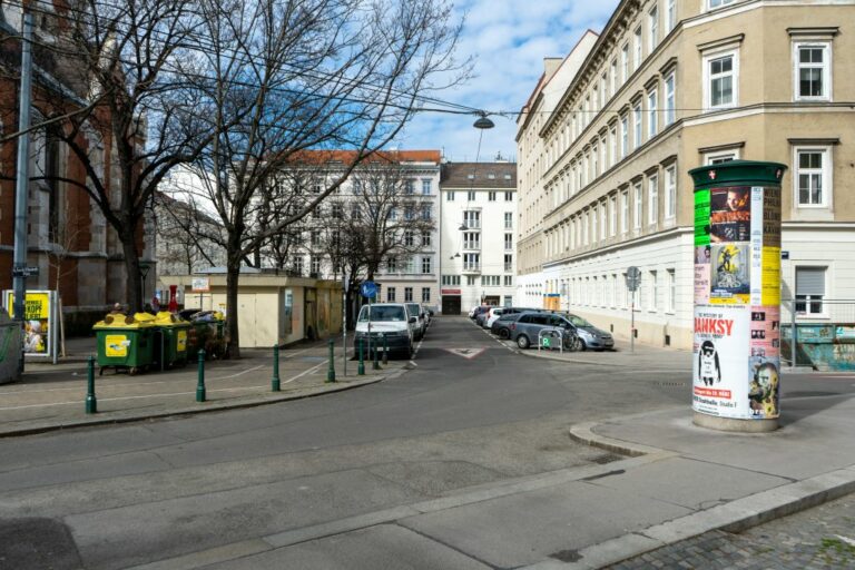 Platz in Wien-Wieden, Bäume, Mistkübel, Poller, Autos, Litfaßsäule, Häuser