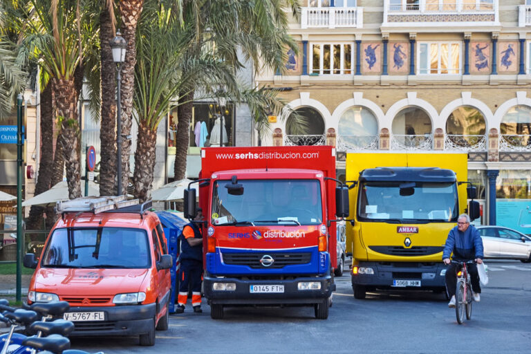 Plaça de la Reina, parkende Kfz auf einem Platz in Valencia, Radfahrer, Palmen, altes Gebäude mit Fassadenschmuck