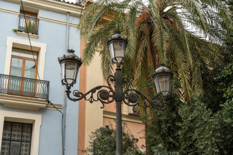 Laterne mit drei Leuchtkörpern vor einer Palme und alten Häusern im Zentrum von Valencia