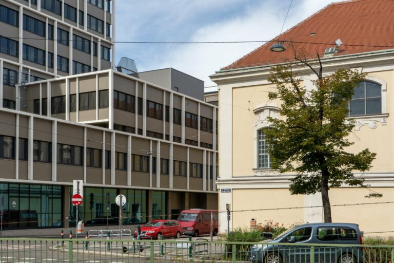 umgebautes Bürohaus neben alter Kirche in Wien, Baum, Autos, Geländer, Oberleitungen