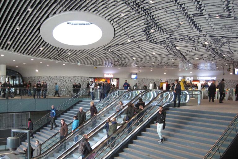 Bahnhof von Delft, Rolltreppen, Treppen, Personen, rundes Dachfenster, Geschäfte, Lamellendecke