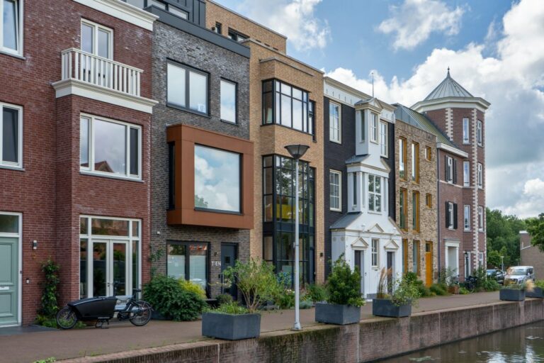 Zeile mit Neubauten in unterschiedlichen Stilen in Delft, vorne ein Kanal