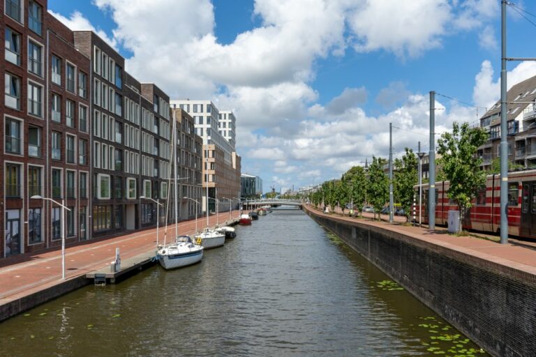 Kanal mit Booten, links neue Gebäude, rechts Straßenbahn und Bäume