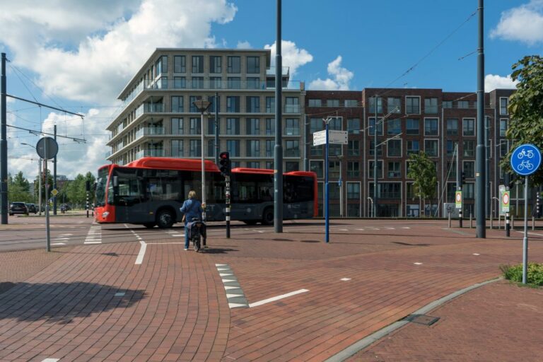 Radfahrerin wartet an einer roten Ampel, Bus fährt über die Straße, Radweg, Wohnhäuser