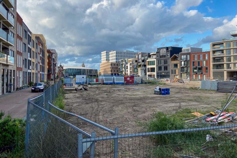 Park wird gebaut, links und rechts Zeilen mit Neubau-Wohnhäusern, hinten Bahnhof und Rathaus