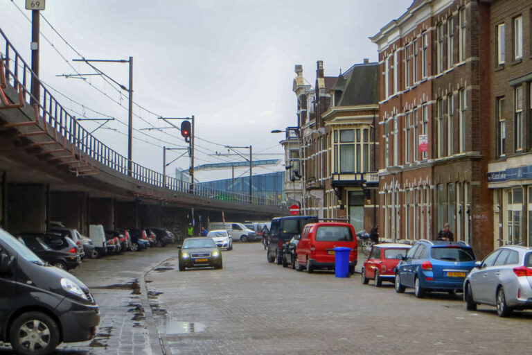 Bahnviadukt neben einer Häuserzeile, fahrende und parkende Autos