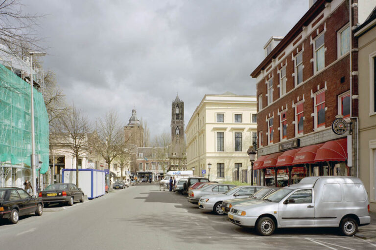 Straße mit parkenden Autos, alten Häusern und Kirchturm