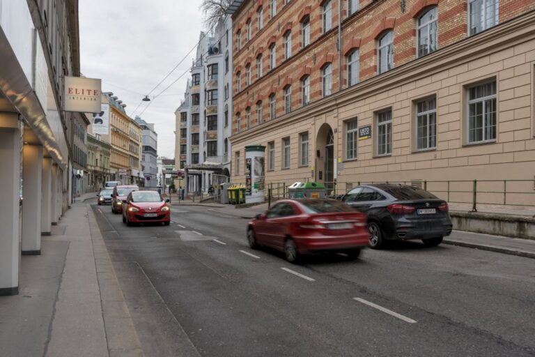 Autos fahren an einem alten Haus mit Sichtziegelfassade und an einem Wohnhaus der Postmoderne vorbei