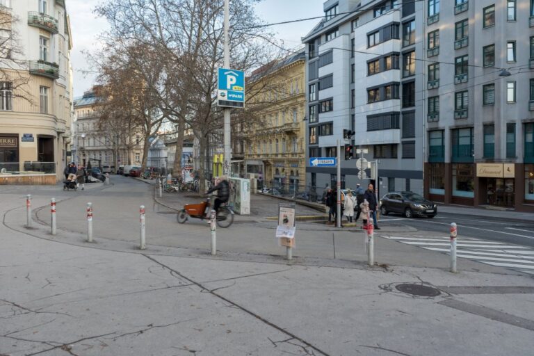 Radfahrer fährt über den Fritz-Grünbaum-Platz in die Windmühlgasse, Fußgänger warten an roter Ampel, Bäume im Winter