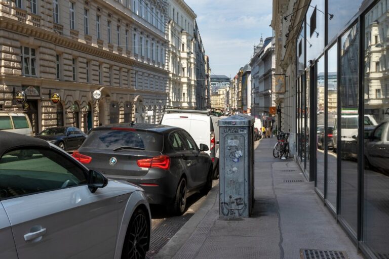 Schaltkasten auf einem Gehsteig in der Gumpendorfer Straße neben parkenden Autos und einem Schaufenster