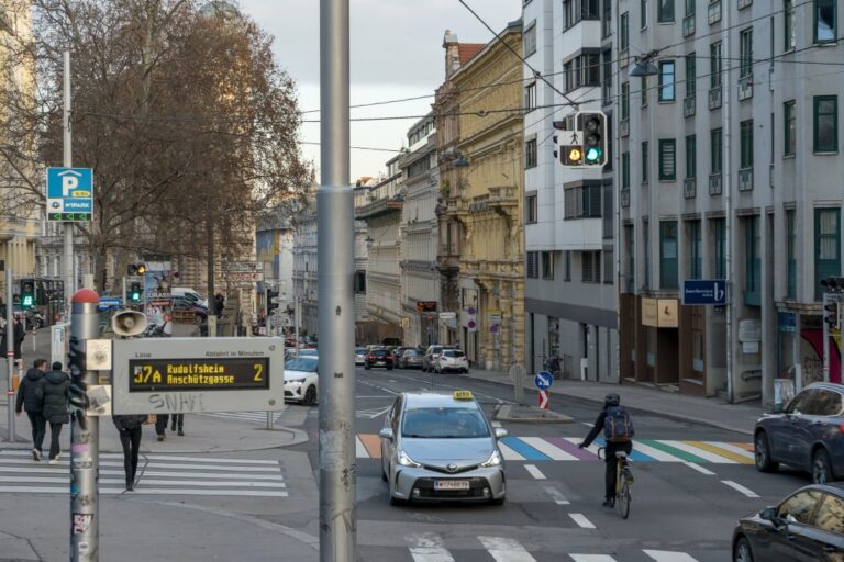 Kreuzung in Mariahilf, Autos, Taxi, Radfahrer biegt ab, Fußgänger gehen über einen Zebrastreifen, Anzeige der Linie 57A, Ampel, Häuser