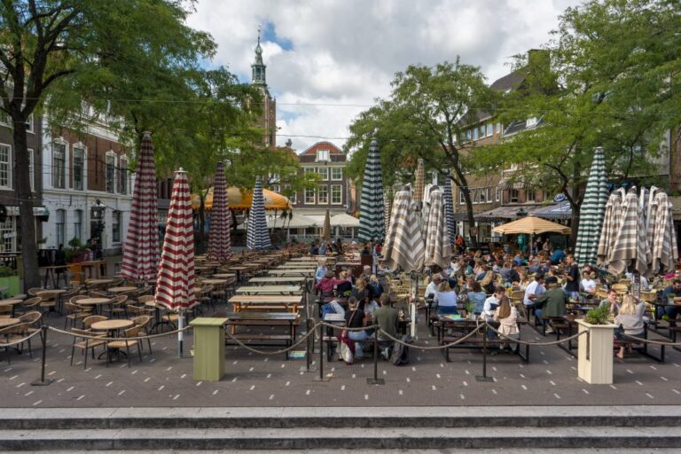 Platz in Den Haag, Tische, Schirme, Bäume, Turm einer Kirche