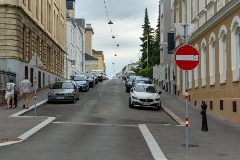 steile Straße in Döbling mit parkenden Autos, Verkehrszeichen und alten Häusern