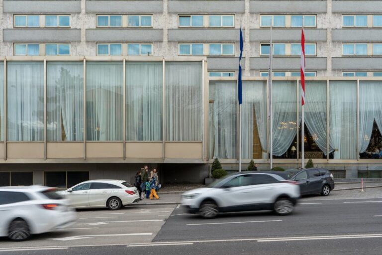 Autos fahren vor einem Hotel vorbei, Fußgänger, Fahnen