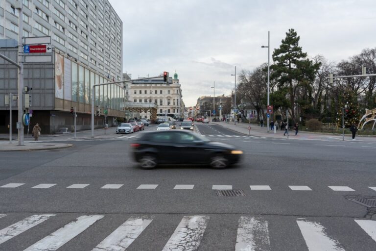 Auto fährt über eine Kreuzung, links Hochhaus, rechts Park