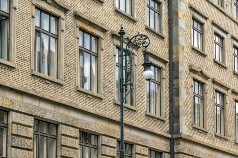 alte Straßenlaterne mit Jugendstildekor vor einem historischen Gebäude mit Klinkerfassade in Tschechien