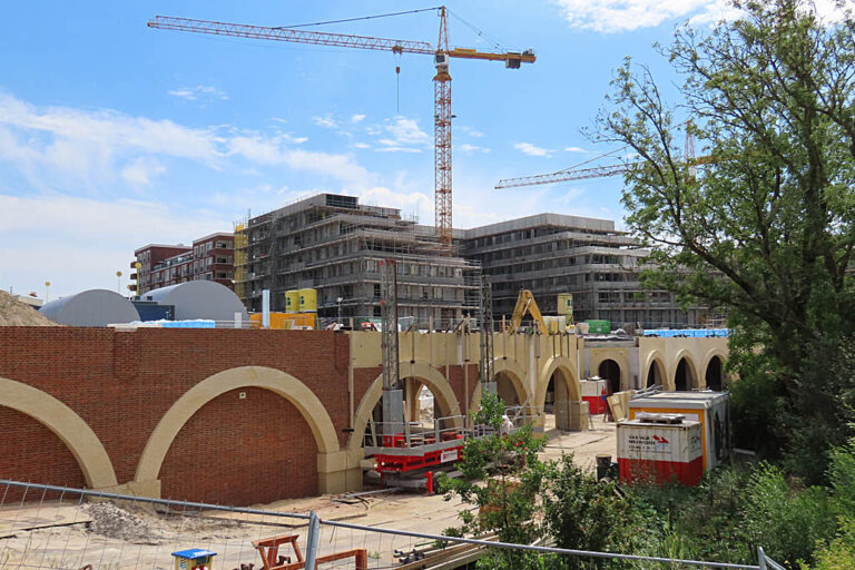 Baustelle in Utrecht, Kran, eingerüstete Gebäude, Bäume, Sträucher, Bauzaun