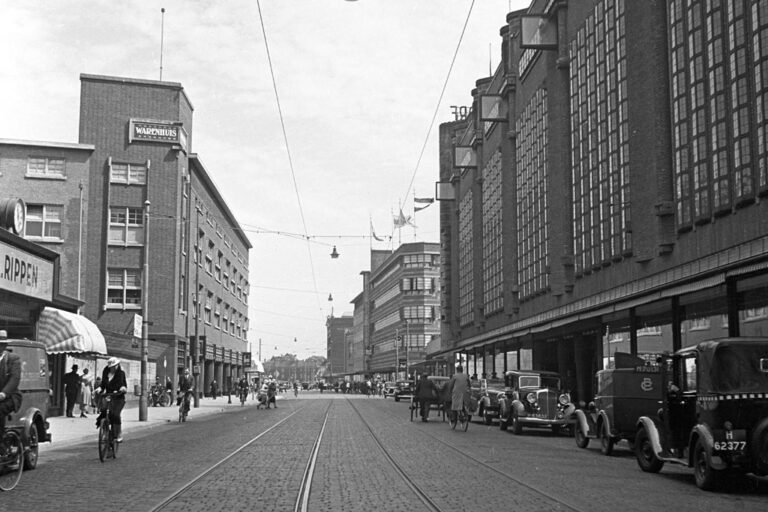 alte Aufnahme einer Einkaufsstraße, rechts parkende Autos