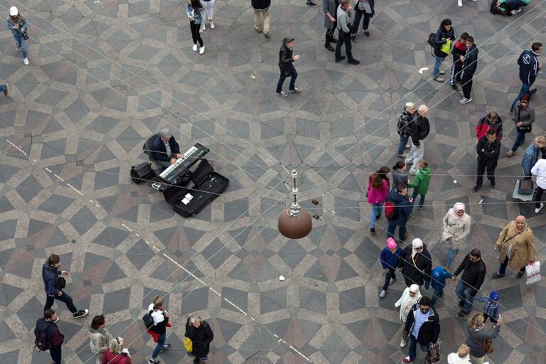 Klavierspieler in einer Fußgängerzone, Leute, hängende Lampe, Pflasterbelag mit Muster